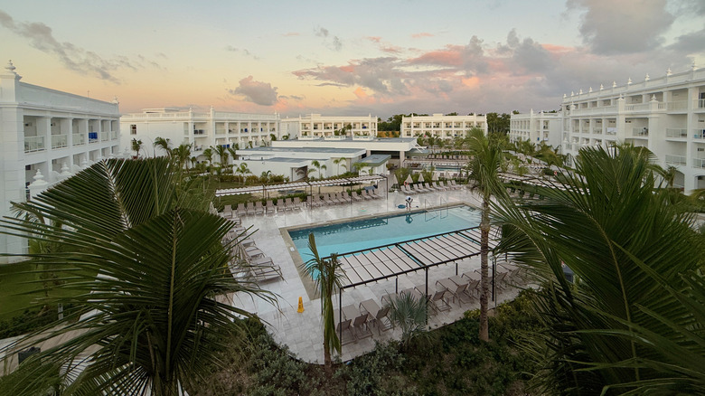 Aerial shot of white hotel rooms surrounding a swimming pool and palm fronds