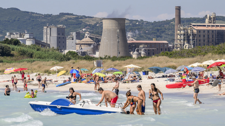 People playing in the shallow water of a beach with the chemical plant in the background